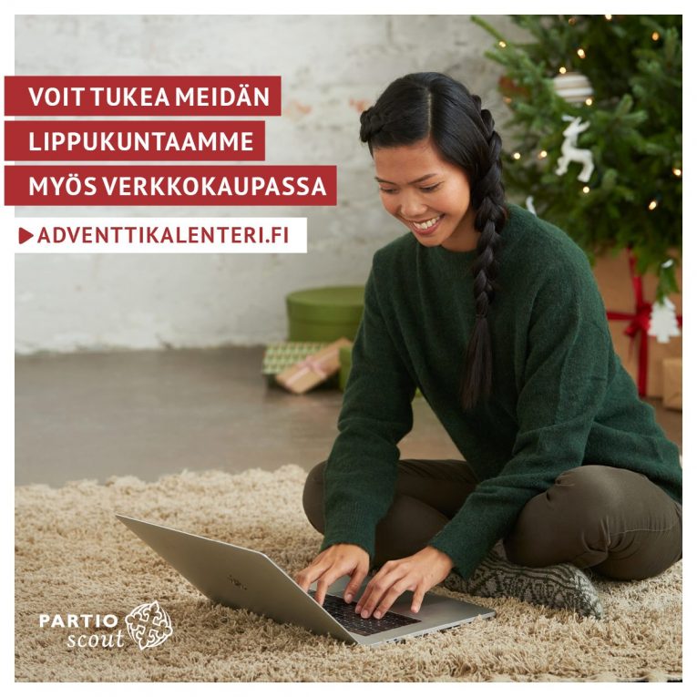 Valokuva jossa ihminen istuu lattialla tietokoneen edessä. Teksti: Voit tukea meidän lippukuntaamme myös verkkokaupassa adventtikalenteri.fi