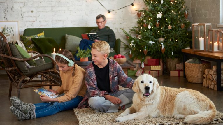 Jouluinen tunnelma huoneessa, jossa kaksi lasta, aikuinen ja koira sekä joulukuusi ja partiolaistena adventtikalenteri