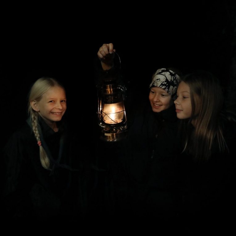 Kolme tyttöä pitelee palavaa myrskylyhtyä pimeässä.